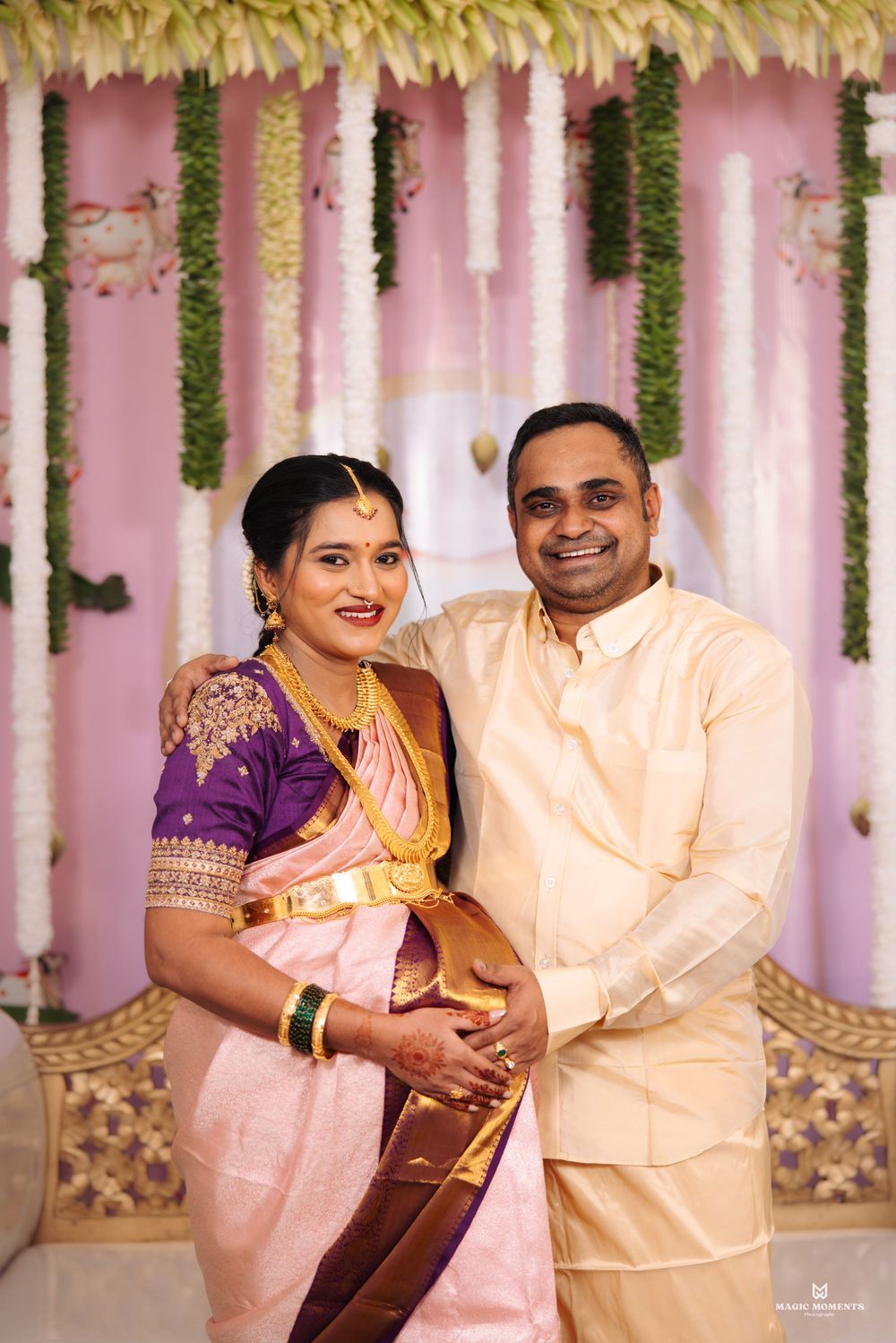 Indian couple in traditional attire posing at a wedding ceremony with floral backdrop.