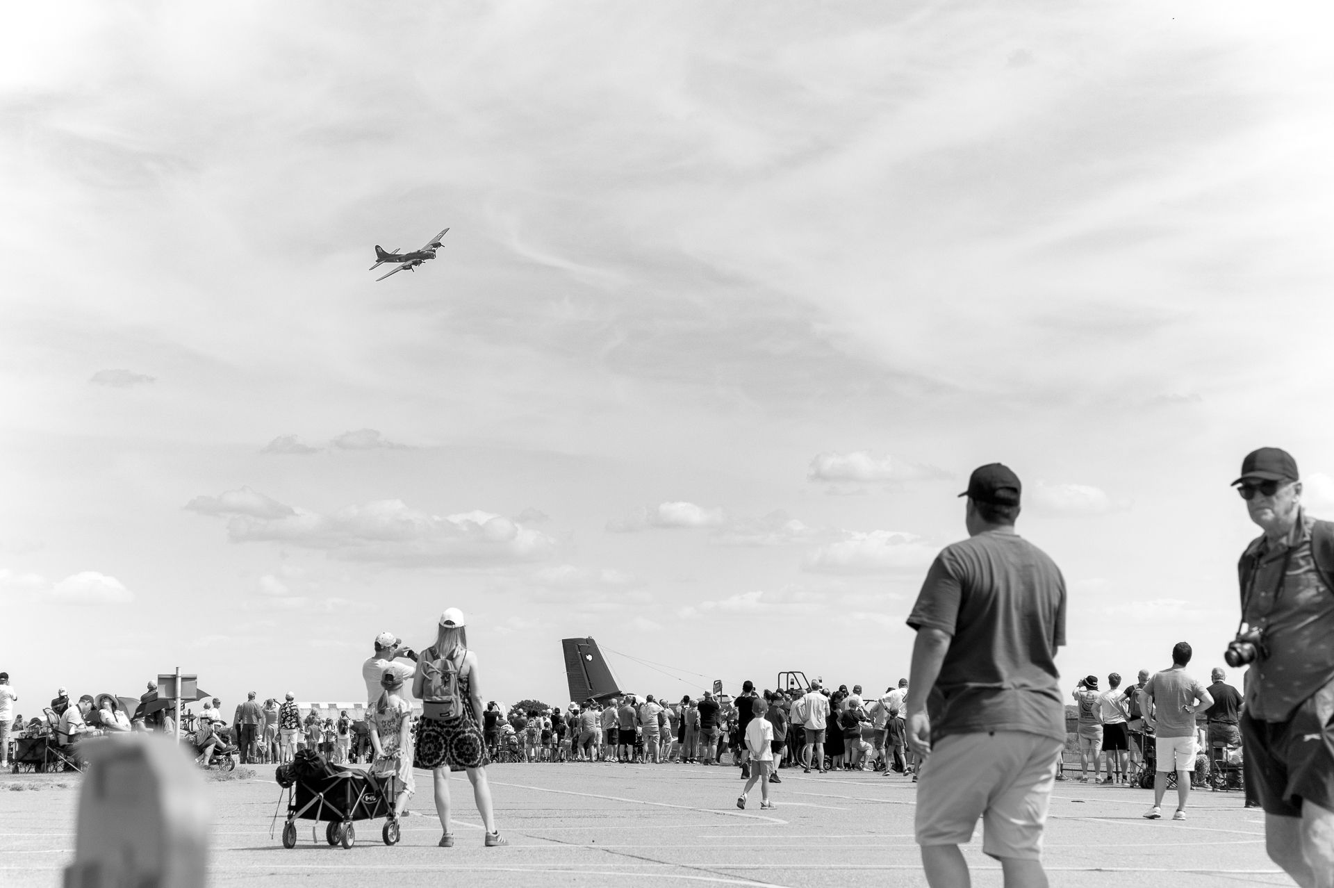 Black and white photo of crowd watching airshow with planes flying overhead on a sunny day.