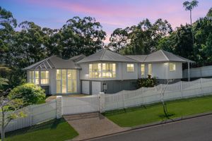 Elegant white Queensland home exterior at twilight with manicured lawn and double garage entrance.