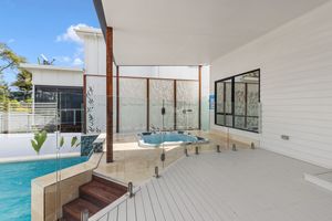 Stylish outdoor entertaining area with pool, spa, glass balustrade, and timber decking.