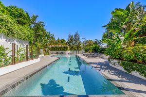 Luxurious lap pool surrounded by tropical palm trees and lush greenery on a sunny day.