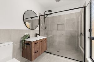 Contemporary bathroom with timber vanity, round mirror, black fixtures, and glass-enclosed shower.