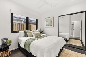 Stylish bedroom with white bedding, mirrored wardrobe, ceiling fan, and dark-framed windows.