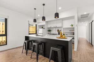 Modern kitchen with black island bench, white cabinetry, pendant lights, and bar stools on timber floors.