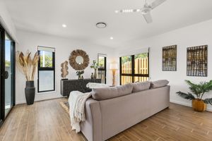Bright living room with grey sofa, timber floors, ceiling fan, and decorative wall art and mirror.