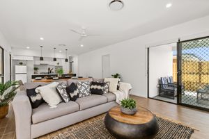 Open-plan living area with grey sofa, timber floors, kitchen view, and sliding door to alfresco.