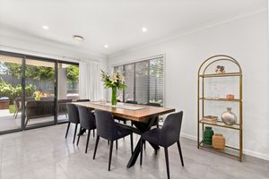 Modern dining room with wooden table, dark chairs, gold shelving unit, and garden views.