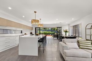 Open-plan kitchen and living area with white cabinetry, island bench, and gold pendant lights.