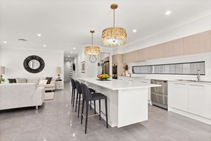 Modern open-plan kitchen with white island bench, gold pendant lights, and bar stools flowing into living area.