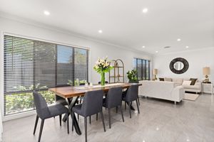 Modern open-plan dining and living room with marble floors, gray chairs, wooden table, and large windows with blinds.