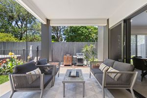 Covered outdoor alfresco entertaining area with gray lounge furniture, BBQ, and lush garden views.