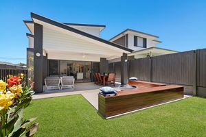 Backyard of modern home featuring green lawn, timber deck with spa, and retractable pergola awning.