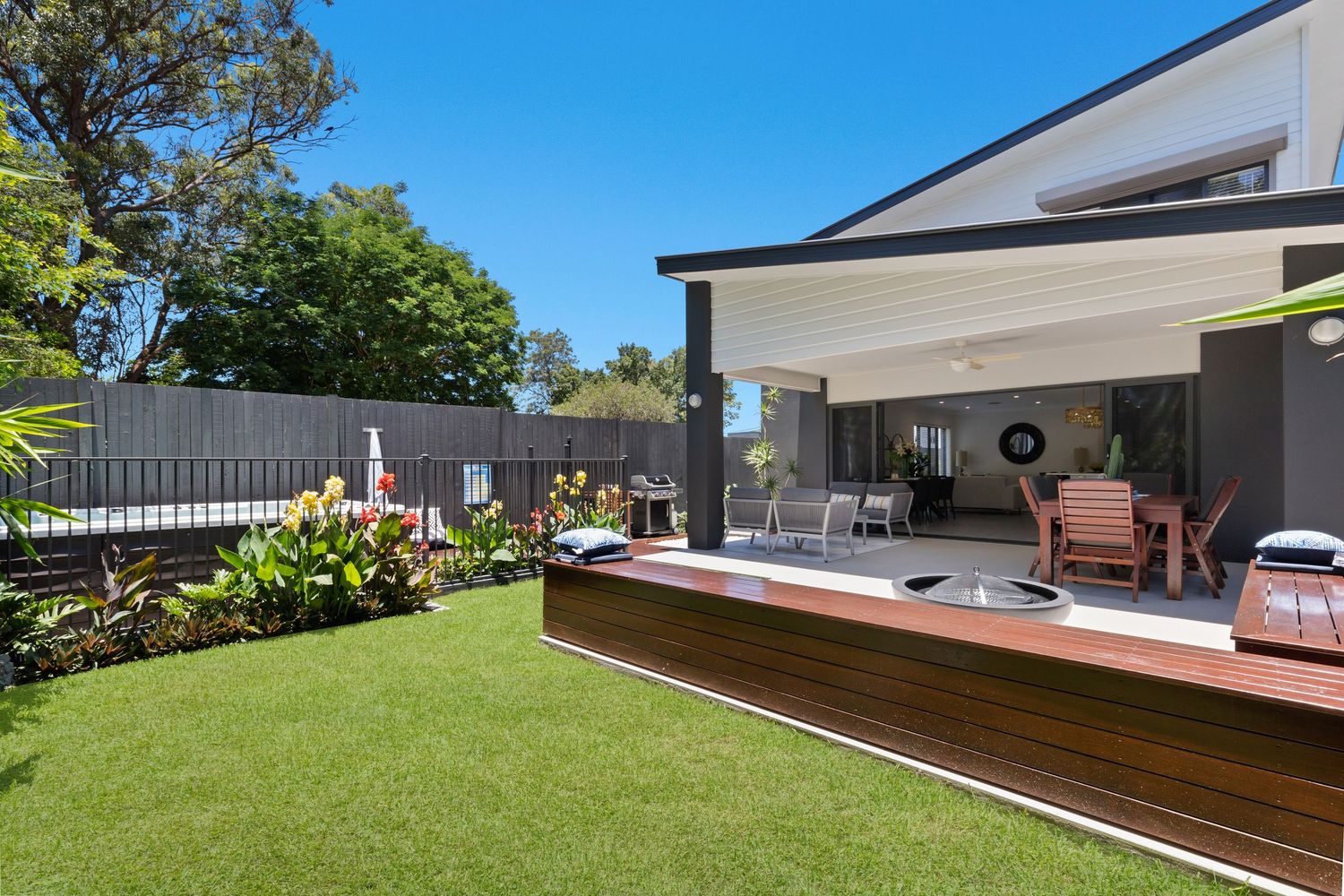 Modern two-story home exterior with large lawn, timber deck, retractable awning, and outdoor dining.