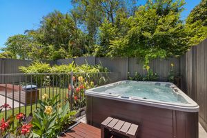 Outdoor spa hot tub on timber deck surrounded by tropical garden plants and gray fencing.