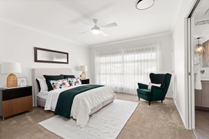 Elegant master bedroom with green velvet armchair, floral bedding, ceiling fan, and sheer curtains.