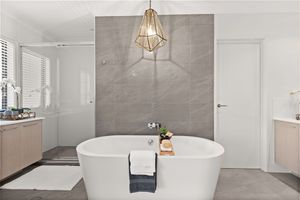 Luxurious bathroom with freestanding white soaking tub, large gray tiles, and geometric gold pendant light.