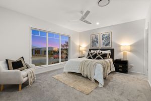 Spacious master bedroom with plush carpet, ceiling fan, large window with evening view, and bedside lamps.