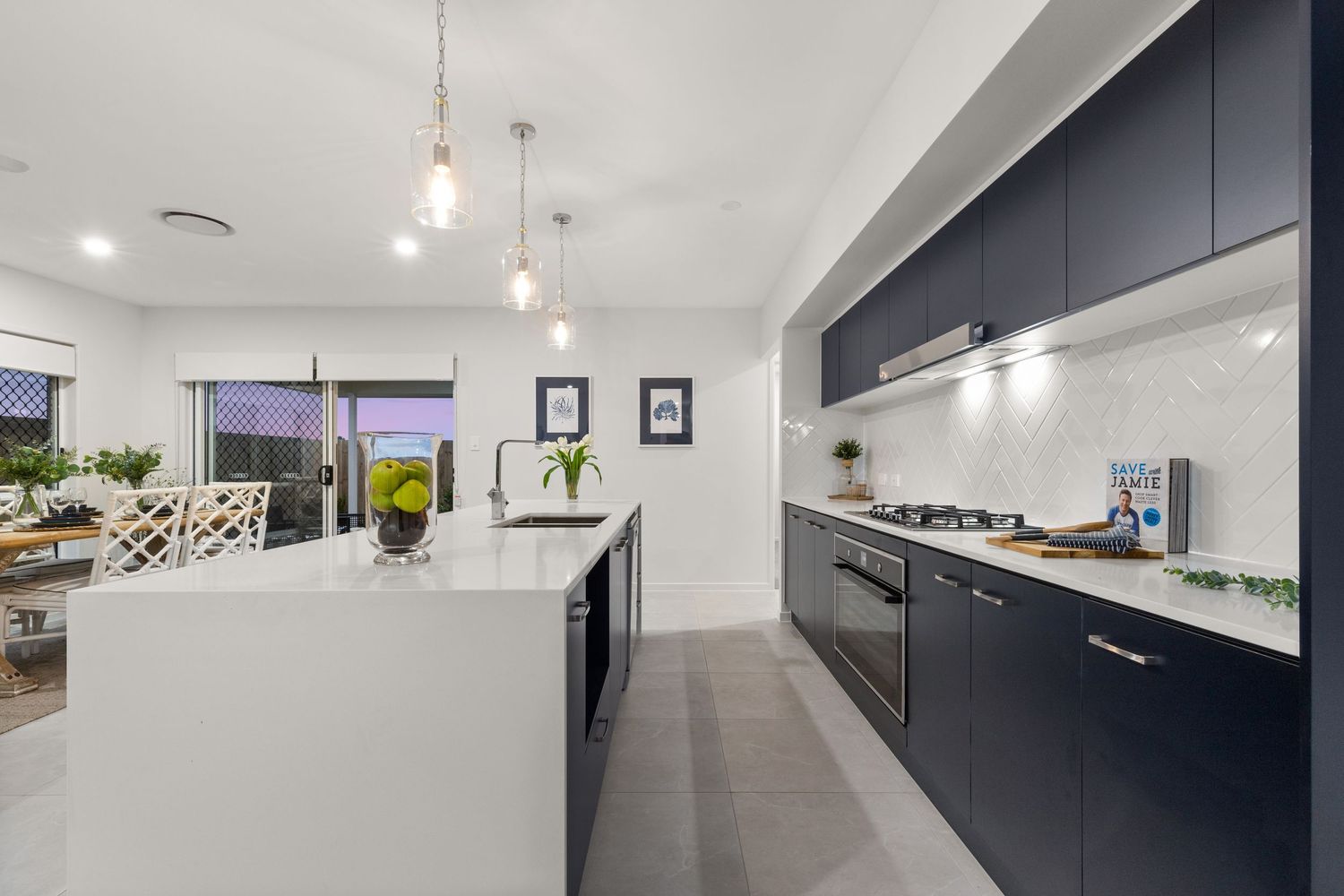 Modern kitchen with navy blue cabinetry, white marble island bench, and pendant lighting over sleek benchtops.