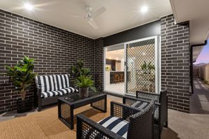 Covered outdoor alley with dark brick walls, striped cushioned seating, and tropical potted plants.