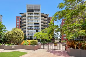 Multi-storey residential apartment complex surrounded by mature tropical trees and gated grounds.