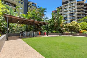 Outdoor entertaining area with pergola, seating, and green lawn within a residential apartment complex.