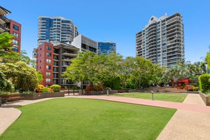 Urban park with manicured lawn and tall modern apartment towers in a sunny city precinct.