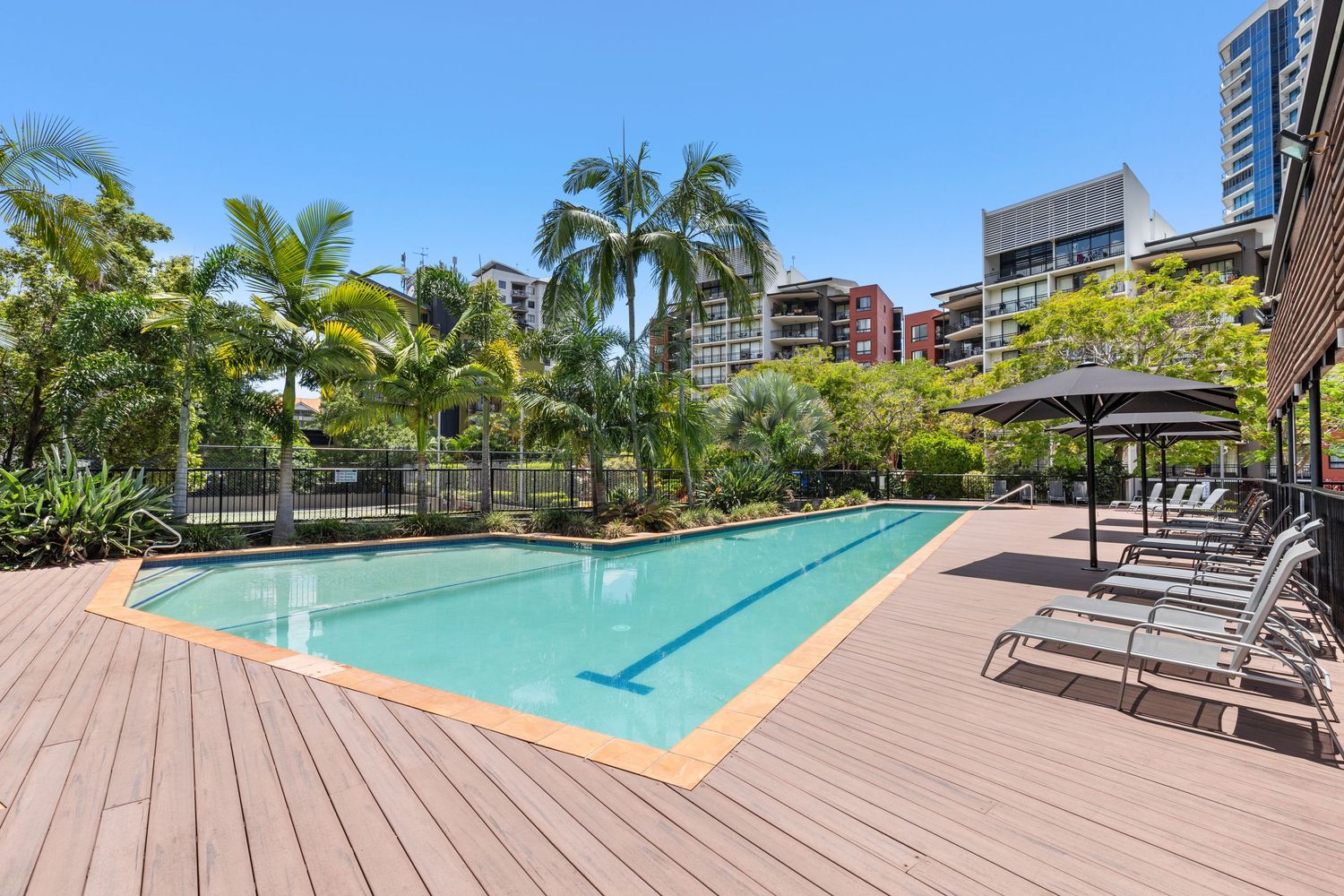 Resort-style outdoor swimming pool with timber decking, sun loungers, and lush tropical landscaping.