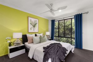 Bedroom with yellow-green accent wall, ceiling fan, dark curtains, and lush garden view.