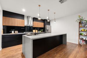 Modern kitchen with black cabinetry, timber accents, concrete island, pendant lights, and hardwood floors.