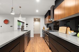 Sleek modern kitchen with dark cabinetry, timber accents, white countertops, and pendant lighting.