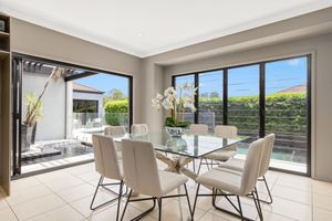 Bright dining room with glass table, cream chairs, and large sliding doors to outdoor pool area.