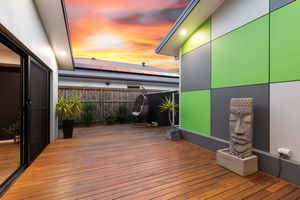Stylish outdoor deck with green and grey feature wall, hanging chair, and decorative stone statue.