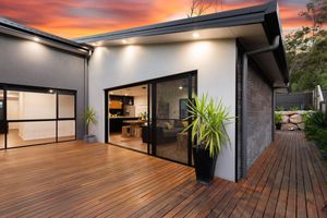 Expansive timber deck with sliding glass doors opening to a modern kitchen at sunset.