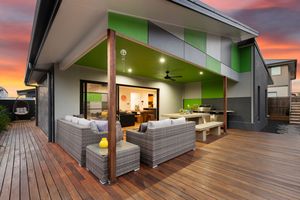 Alfresco entertaining area with grey outdoor lounge, green ceiling, and timber decking at dusk.