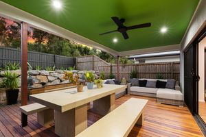 Covered outdoor entertaining area with green ceiling, timber deck, dining table, and lush garden backdrop.
