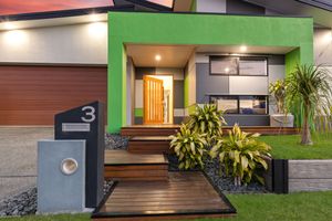 Contemporary home entrance featuring green accent wall, timber pathway, and tropical landscaping at dusk.