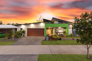 Modern single-story home with bold green facade, double garage, and manicured lawn at sunset.