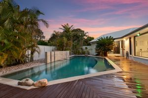 Tropical backyard pool with timber decking, palm trees, and vibrant sunset sky.