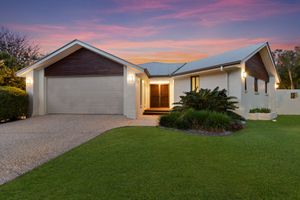 Charming suburban home with double garage, gravel driveway, and green lawn at sunset.