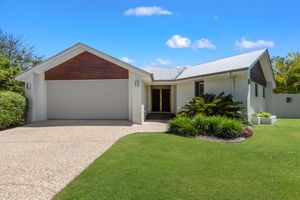 Modern white home with timber accents, double garage, gravel driveway, and lush green lawn under a clear blue sky.