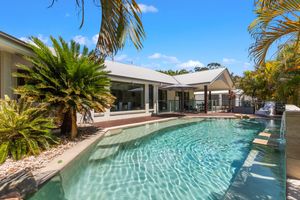 Stunning outdoor swimming pool surrounded by tropical palms and a modern white home in a sunny Australian setting.