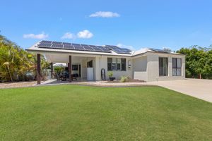 Modern single-story home with solar panels, covered patio, and lush green lawn under a bright blue sky.