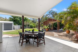 Covered outdoor patio with dining set overlooking lush backyard garden, pergola, and tropical landscaping.