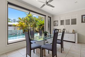 Modern dining area with glass table, dark chairs, pool view through large window, and white sideboard.