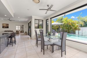 Open-plan dining area with glass table, pool views, and indoor-outdoor living space featuring tile floors and ceiling fan.