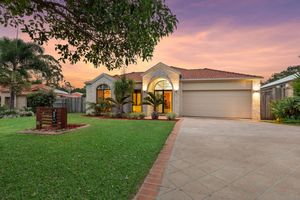 Classic brick home with arched windows, double garage, and green lawn at sunset.