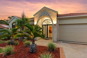 Elegant home entrance with stone archway, palm tree, and decorative landscaping at dusk.