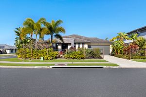 Single-storey suburban home with tropical palm trees, lush gardens, and double garage on quiet street.