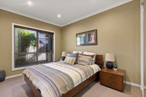 Cozy bedroom with striped bedding, timber furniture, carpet flooring, and venetian blind window.
