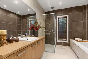 Modern bathroom with dark tile walls, timber vanity, glass shower, and freestanding bathtub.